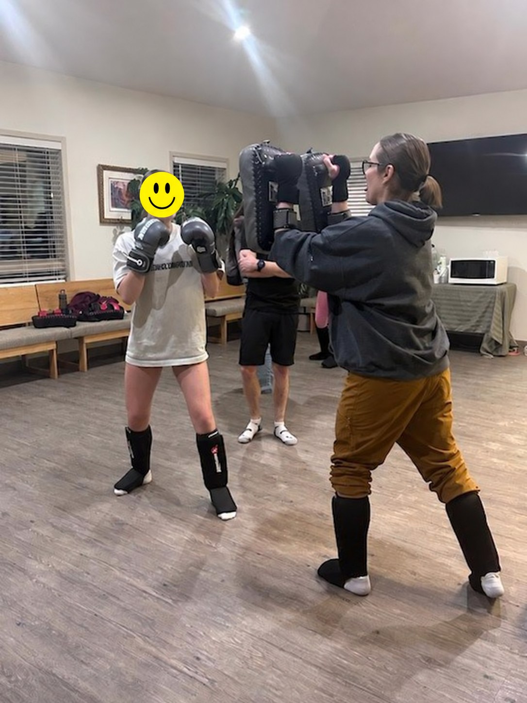 A participant practising controlled Muay Thai padwork, with the minor participant's face covered by a smiley graphic